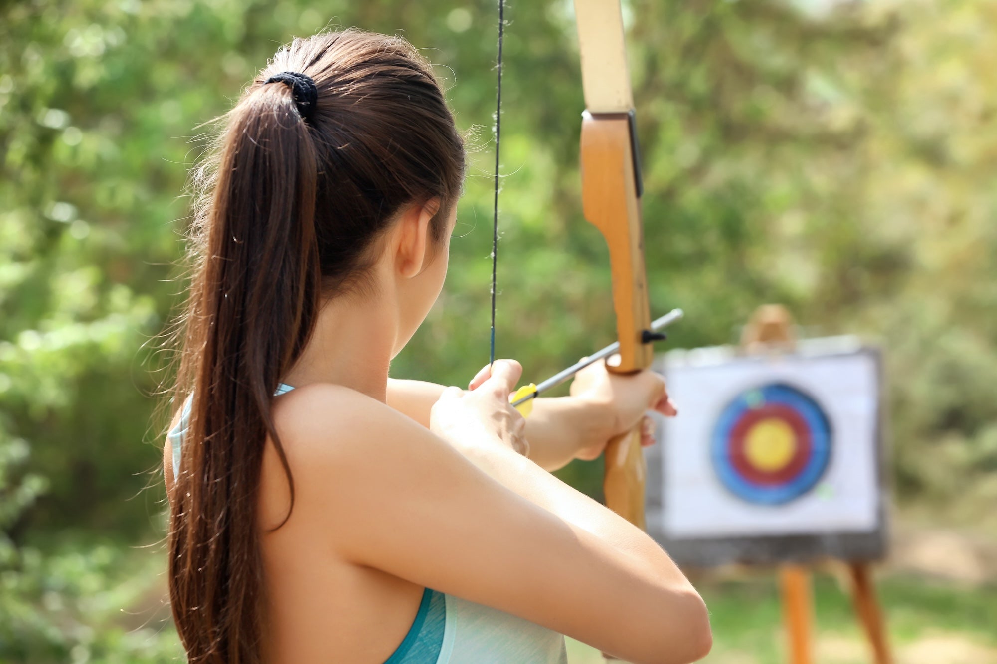 Archer aiming a bear bow recurve at a target during outdoor archery practice.