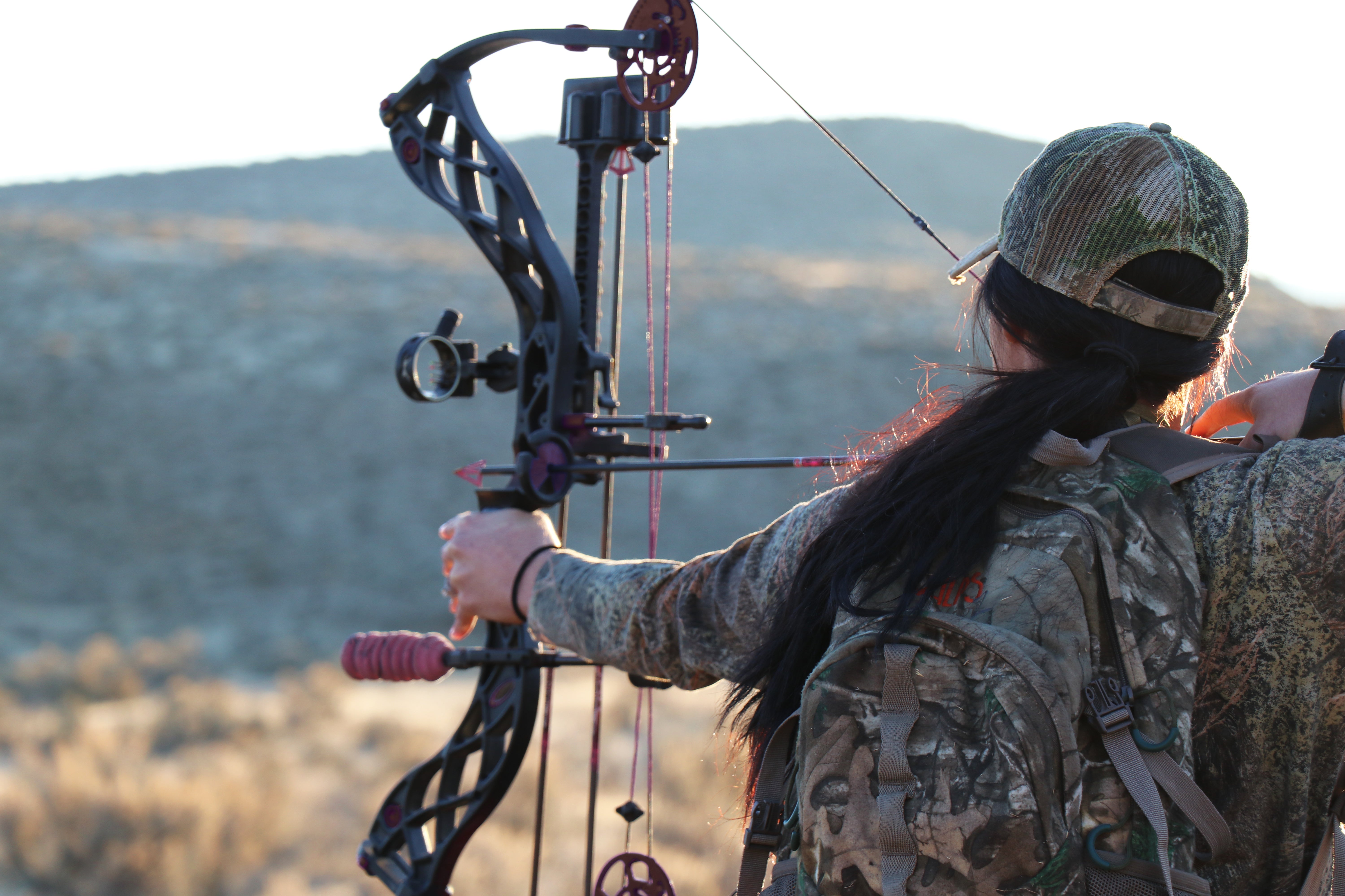 Female hunter aiming a streamlined black Hoyt bow with integrated accessories and stabilizer during an outdoor hunt.